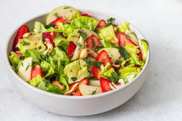 Fresh salad with lettuce leaves, apples, strawberries and cashew nuts