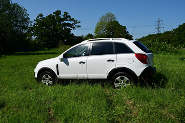 White SUV parked in a long grass field in the English countryside in summer time. 