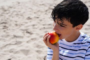 preteen boy, eating a red apple in the summer at the beach