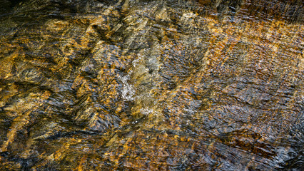 A close-up of water flowing over a granite creek bed with rich, warm, browns, golds, and yellows. Abstract nature.