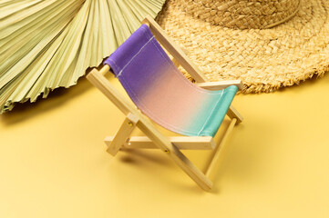 Colorful beach chair, straw hat, dried palm leaf on yellow background. Summer, holidays and beach...