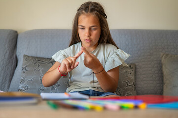 9 Year Old School Girl Doing Homework At Home, She Is Adding With Her Fingers To Do Math Exercises....
