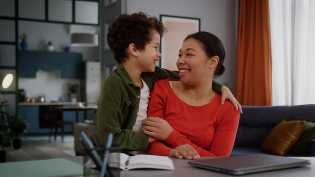 Happy African American family smiling laughing freelancer woman mother female girl with little multiracial kid child adopted son boy talking laugh cuddling at home table with laptop love relationship