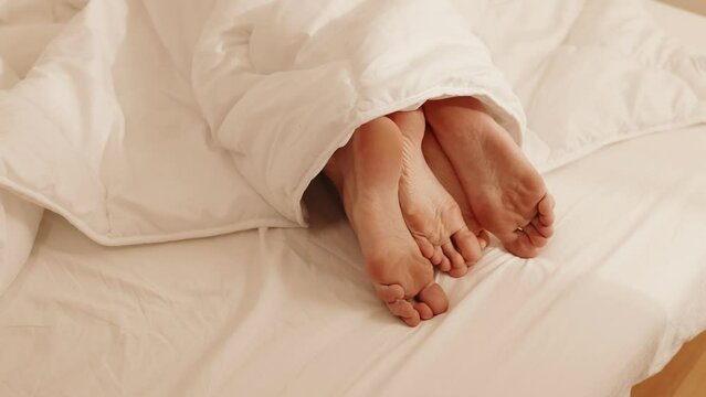 Close-up image of a couple's feet intertwined under a warm blanket, conveying love, intimacy, and a cozy atmosphere.