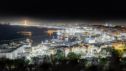 Algiers, Algeria- April 19, 2024: aerial view on the capital city by night sea bay and pier port, Mediterranean sea water ships and boats. The Great mosque and the Martyr's Memorial monument.