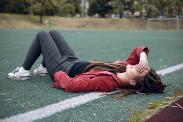 A happy teen girl lies on the grass on the playground. Daytime, stadium, open air