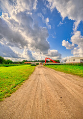 Big clouds passing over a red excavator in a rustic landscape in The Netherlands.