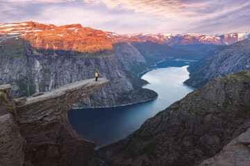 A tourist in a yellow jacket stands on the edge of the Troll's Tongue (Trolltunga) rock in Norway....