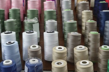 There are many spools of thread of different colors for sewing clothes, standing ready for work.