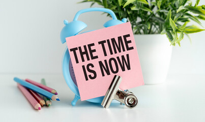 Paper note word The Time Is Now on alarm clock desk white background. Sticker note paper message...