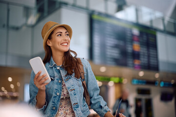 Happy traveler using cell phone while waiting for her flight at airport.