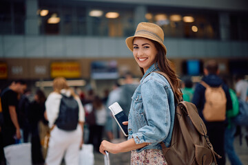 Happy traveler waiting for her flight at  airport and looking at camera.