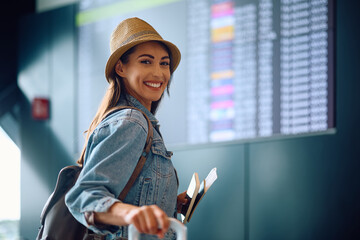Young happy woman checking her flight schedule at airport and looking at camera. © Drazen
