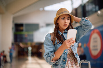 Young shocked woman using mobile phone at airport.