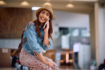 Happy female traveler talking on phone at departure area.