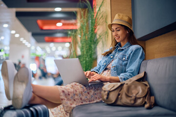 Smiling female traveler surfing  net on laptop at departure area