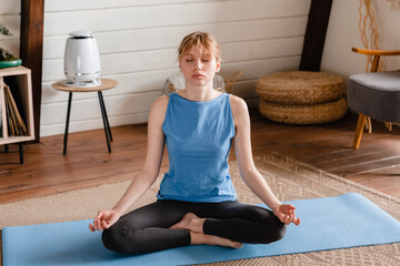 Concentrated serene young caucasian woman meditating on exercise mat sitting in lotus yoga position...