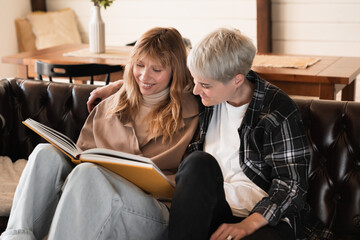 Two young caucasian lesbians romantic LGBT couple watching photoalbum, remember happy moments on...