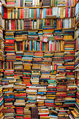 Large amount of books stacked on top of each other in room.