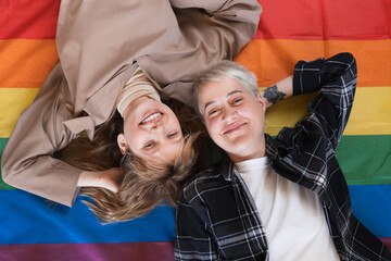 Loving transgender lesbian couple two girlfriends lying on rainbow LGBT flag together protesting...