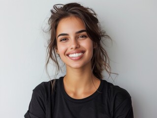 Fototapeta premium Beautiful natural brunette woman, smiling and looking in camera with white teeth. Close-up portrait of cute female woman in black t-shirt on white background. 