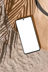 Aesthetic tropical summer business branding template, mobile phone empty screen mockup, straw hat on sand beach texture background with natural palm tree foliage sunlight shadow
