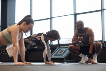 Side view portrait of people doing plank exercise with Black man as coach assisting in training
