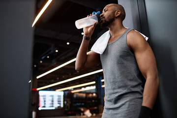 Side view portrait of muscular Black man drinking water after training in gym interior, copy space