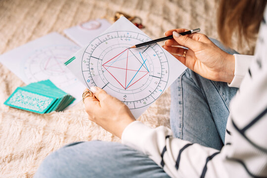 Tarot reader reads natal chart with tarot cards while sitting on bed.