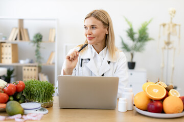 Mature dietitian working with laptop computer making balanced corrective diet plan for patient or...