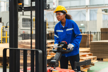 African American female worker driving forklift truck in heavy metal industrial factory, Smiling woman engineer wearing vest and helmet safety moving material at warehouse factory © chokniti