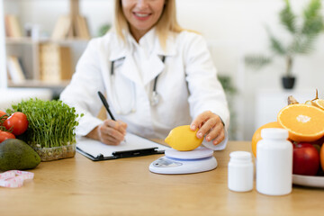 Close up of hands of female nutritionist doctor sitting at table with vegetables and fruits in...