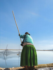 A Peruvian woman standing on a boat fishing with a pole on Lake Titikaka.