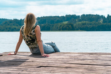 A girl sits on a wooden bridge by the lake in warm summer weather. Thinking one on one with nature.