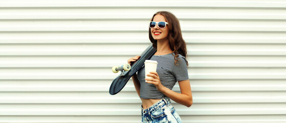 Portrait of stylish young woman with skateboard and cup coffee on white background