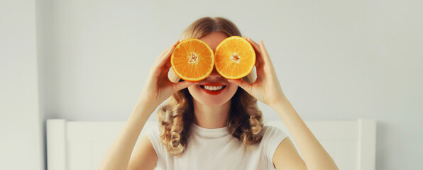 Happy healthy cheerful young woman covering her eyes with slices of orange fruits and looking for