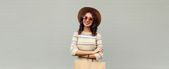 Stylish beautiful happy smiling young woman posing with shopping bags in round hat, gray background