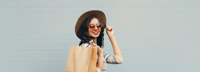Stylish beautiful happy smiling young woman posing with shopping bags in round hat, gray background