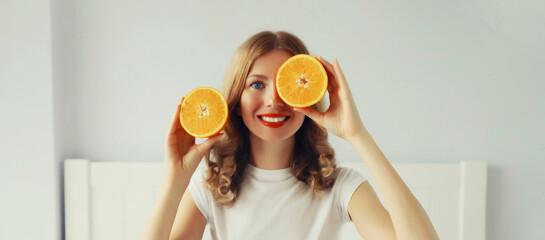 Happy healthy cheerful young woman with slices of orange fruits in white room at home