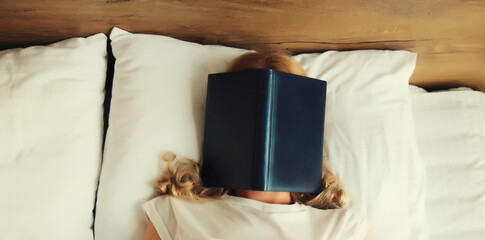 Young sad tired woman student with open book lying on the bed at home