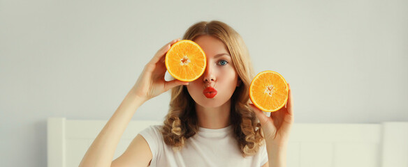 Happy healthy cheerful young woman with slices of orange fruits in white room at home