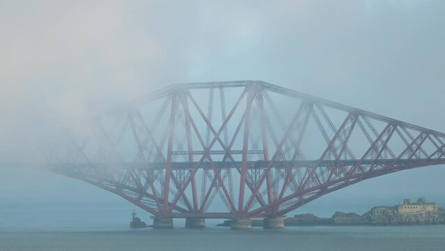 A train travelling over a railway bridge covered in thick fog. Forth Bridge, Scotland, United Kingdom