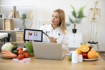Skillful female nutritionist explaining details of slimming program for client online. Focused...
