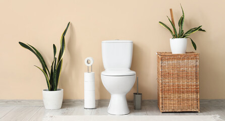 Interior of restroom with toilet bowl, basket and houseplants near beige wall