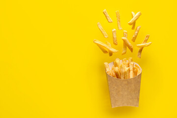 Paper box with tasty french fries on yellow background