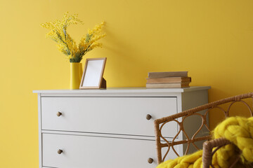 Cabinet with armchair and knitted blanket near yellow wall