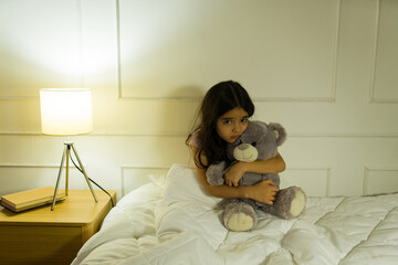Cute little girl embraces her teddy bear tightly while feeling scared of bad dreams at night in her...