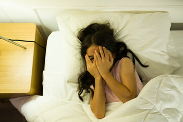 Hispanic girl in bed covering her eyes with her hands, evoking feelings of fear or timidity at home