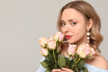 Pretty young woman with bouquet of beautiful roses on grey background