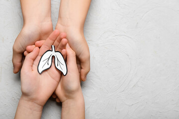 Hands of woman and child with paper lungs on grey background